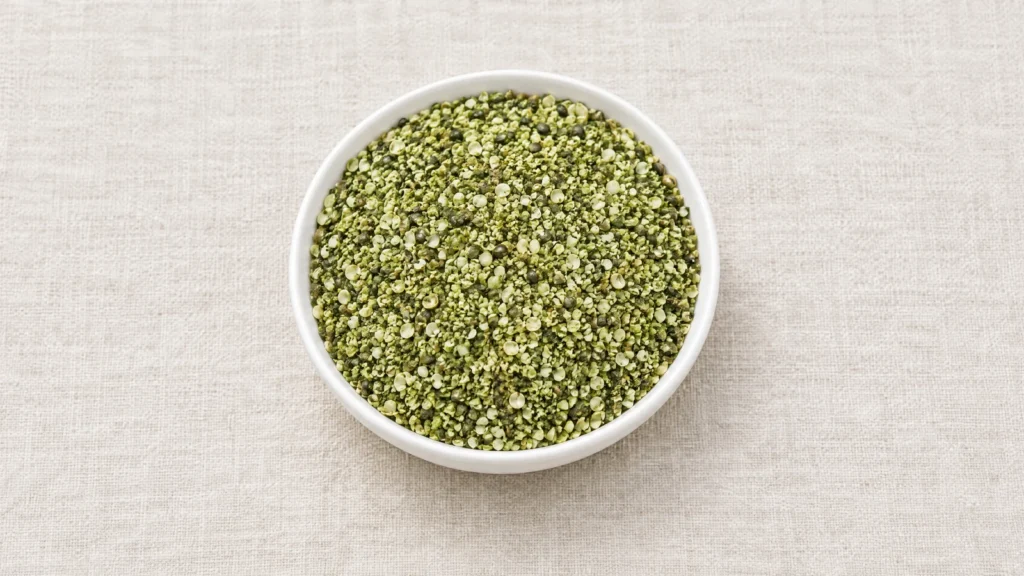Granular smoothie hemp, small green kernel and hull fragments, in a white ceramic dish on linen